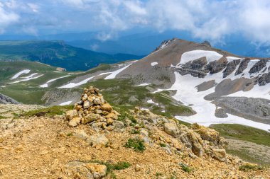 Çiçekli çayırlar ve karla kaplı dağlık tepeleri olan kayan tepelerin manzaralı panoramik manzarası. Güzel güneşli bir gün mavi gökyüzü ve baharda bulutlar.
