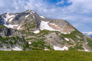 Çiçekli çayırlar ve karla kaplı dağlık tepeleri olan kayan tepelerin manzaralı panoramik manzarası. Güzel güneşli bir gün mavi gökyüzü ve baharda bulutlar.