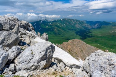 Çiçekli çayırlar ve karla kaplı dağlık tepeleri olan kayan tepelerin manzaralı panoramik manzarası. Güzel güneşli bir gün mavi gökyüzü ve baharda bulutlar.