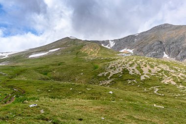 Çiçekli çayırlar ve karla kaplı dağlık tepeleri olan kayan tepelerin manzaralı panoramik manzarası. Güzel güneşli bir gün mavi gökyüzü ve baharda bulutlar.
