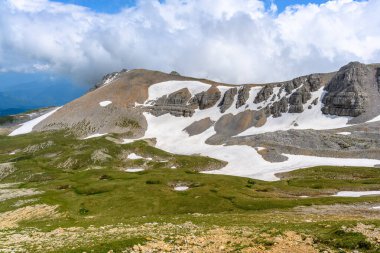 Çiçekli çayırlar ve karla kaplı dağlık tepeleri olan kayan tepelerin manzaralı panoramik manzarası. Güzel güneşli bir gün mavi gökyüzü ve baharda bulutlar.