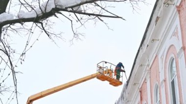 Ulyanovsk, Rusya - 12 Şubat 2024: Asansör kullanarak evin çatısından buz saçakları ve karları temizlemek. Şehir sokaklarında yayalar için tehlikeli durumların önlenmesi.