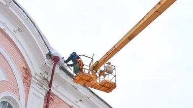 Ulyanovsk, Rusya - 12 Şubat 2022: Asansör kullanarak evin çatısından buz saçakları ve karları temizlemek. Şehir sokaklarında yayalar için tehlikeli durumların önlenmesi.