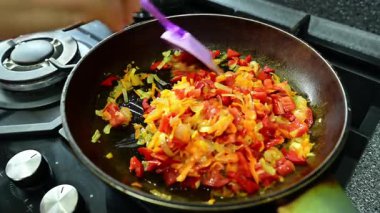Biberler, domatesler, soğanlar ve rendelenmiş havuçlar kızarırken tavada cızırdar, aromaları mutfağı doldurur. Bir spatula karışımı karıştırır, hatta yemek pişirmesini sağlar ve lezzetlidir..