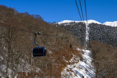 Kış ormanı arka planında teleferik olan bir resim. Karlı yamaçlar ve ip sandalyeler bir kayak merkezi atmosferi yaratır..