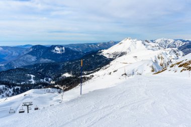 Göz kamaştırıcı bir kış manzarasıyla çevrili, yamaçtan zarif bir şekilde yükselen bir kayak asansörünün yer aldığı karlı bir dağ manzarası.