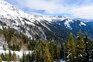 Karla kaplı tepeleri ve ormanlarla kaplı dağları olan bir kayak merkezi. Uzakta bir dağ sırası görünüyor ve önümüzde güzel bir kış manzarası açılıyor..