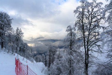 Bir kayak yamacı, koruyucu bir ağ ve dağların manzarası..