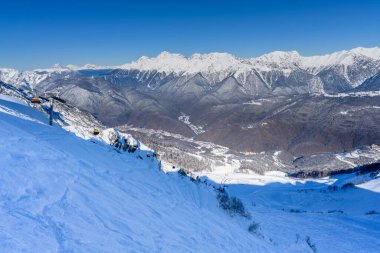 Kayak yamacının tepesinden karla kaplı dağların temiz manzarası. Dağ sırası mesafeye kadar uzanıyor. Soçi 'deki Kafkas Dağları