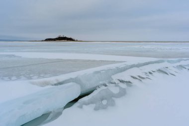 Issız bir ada ve Ulyanovsk yakınlarındaki en geniş ve en derin noktasında donmuş Volga Nehri 'nde büyük bir çatlak. Donmuş bir nehrin, adanın, humuların ve buzun kış manzarası.