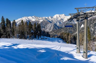 Kış manzarası karşısında teleferikli bir fotoğraf. Karlı yamaçlar, kayak pistleri ve çok sayıda asansör bir kayak merkezinin atmosferini oluşturuyor. Arka planda.