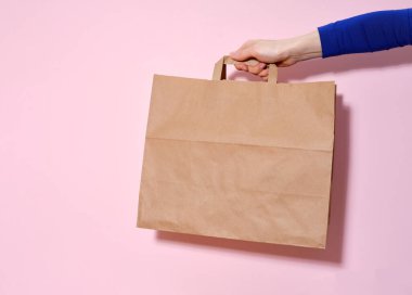Dişi el, bir kese kâğıdı ve teslim edilmiş eşyalar tutuyor. Pembe arkaplan, kopyalama alanı