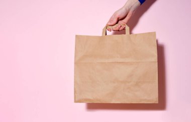 Dişi el, bir kese kâğıdı ve teslim edilmiş eşyalar tutuyor. Pembe arkaplan, kopyalama alanı