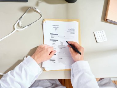 Beyaz önlüklü, kimliği belirsiz bir erkek doktor klinikte tıbbi belgeler dolduruyor.