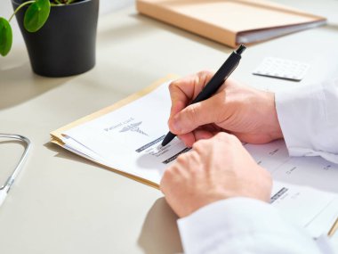 Beyaz önlüklü, kimliği belirsiz bir erkek doktor klinikte tıbbi belgeler dolduruyor.