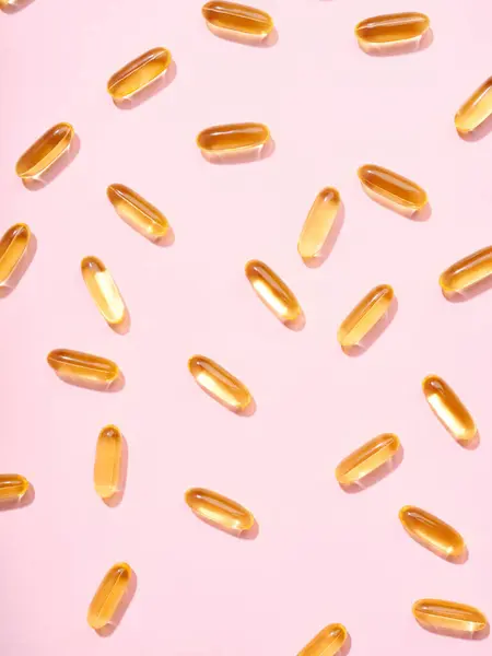 Omega 3平粉色背景的金半透明药丸 图库照片