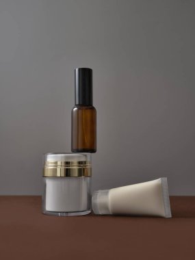 Lüks cilt bakımı seti, kahverengi ve gri arka planda boş güzellik ürünleri şişeleri. Çeşitli aksesuarlarla ürün çekimi. Serum, el kremi, nemlendirici..