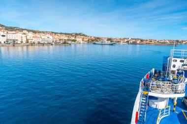 Ferry boat approching La Maddalena shore on a sunny day in autumn. Sardinia, Italy clipart