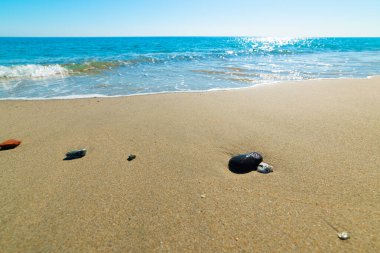 Altında turkuaz su olan altın kumda taşlar olan plaj. Sardunya, İtalya