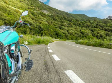 Bulutlu bir gökyüzünün altında bir kır yolunun kenarına park etmiş bir kruvazör motosikleti.