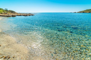 Porto Pirastu sahilinde çakıl taşları ve turkuaz su var. Sardunya, İtalya