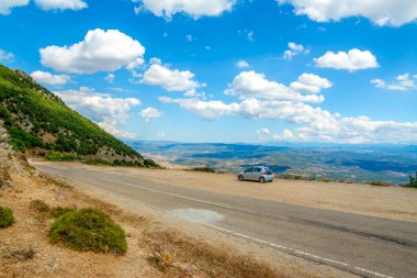 Araba bulutlu bir gökyüzünün altında bir kır yolunun kenarına park edilmiş.