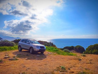 Araba parlayan güneşin altında, deniz kenarında park halinde.