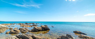 İtalya, Sardunya 'da kayaların üzerinde mavi gökyüzü ve berrak su