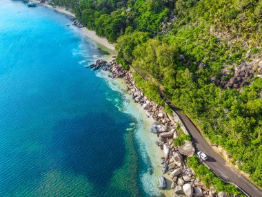 Palmiye ağaçları, granit kayaları ve mavi denizi olan bir sahil yolu. Tropik plaj. Seyşeller, Hint Okyanusu
