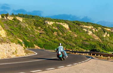 Gün batımında virajlı bir yolda klasik bir motosikletli.