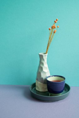 Mor masada bir fincan çay ve bir vazo kuru çiçek. mavi arkaplan