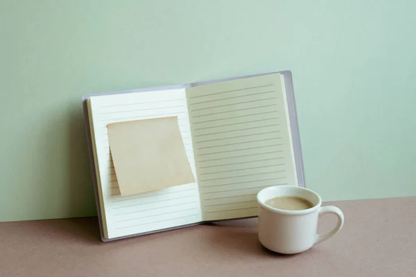 Open notebook and sticky memo pad and cup of coffee on desk. mint wall background. workspace, business, study place