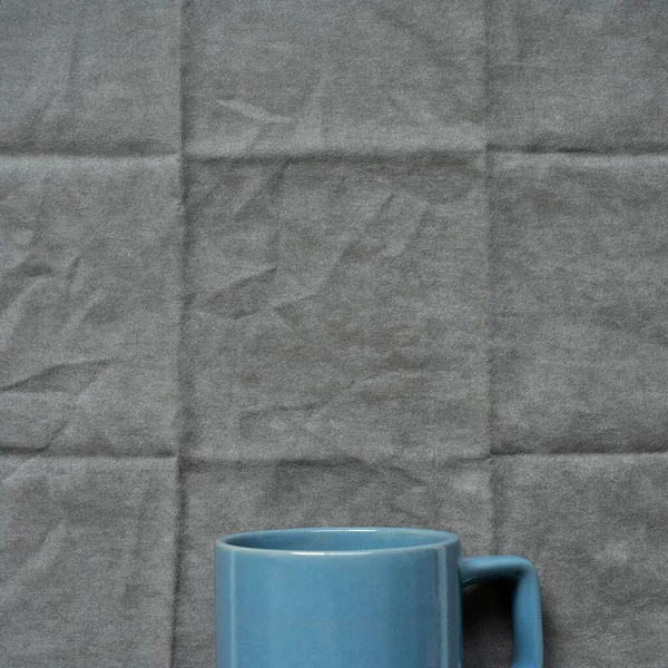 Blue mug cup on gray fabric background. top view