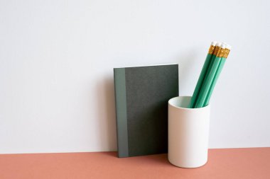 Black notebook and green pencil in holder on red desk. white wall background. minimalism, copy space