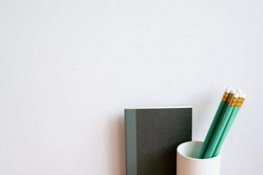 Black notebook and green pencil in holder. white wall background. minimalism, copy space