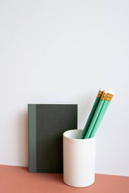 Black notebook and green pencil in holder on red desk. white wall background. minimalism, copy space