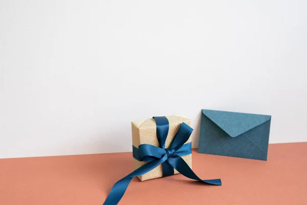 Gold gift box and navy color envelope on red table. white wall background. minimalism, copy space