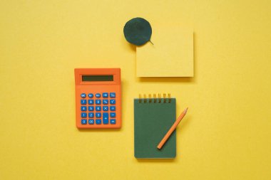Green notepad, memo paper, color pencil, calculator isolated on yellow background. flat lay, top view, copy space