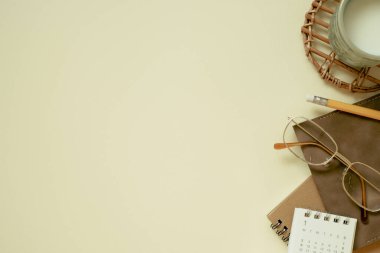 Brown notebook, calendar, eyeglasses, cup of milk, pencil on yellow desk background. flat lay, top view, copy space