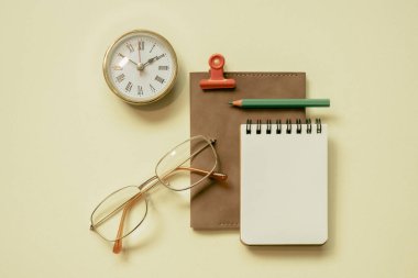 Notepad, diary, clock, eyeglasses, pencil, clip on yellow desk background. flay lay, top view, copy space