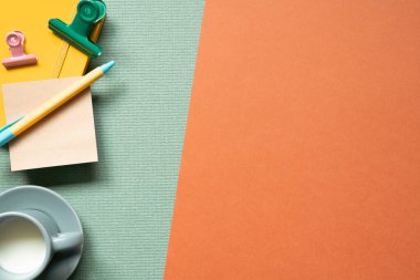 Sarı defter ve kalem, ataç, yeşil ve kırmızı masa arkaplanlı bir fincan süt. Çalışma alanı ve çalışma alanı. düz alan, üst görünüm, kopyala boşluk