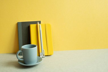 Günlük defter ve kalem, gri masadaki bardak. Sarı duvar arkaplanı. çalışma ve öğrenim yeri