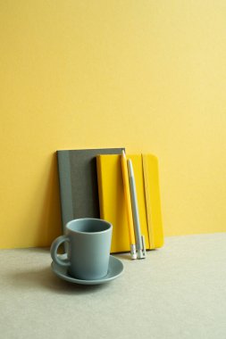Günlük defter ve kalem, gri masadaki bardak. Sarı duvar arkaplanı. çalışma ve öğrenim yeri