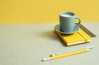 Günlük defter ve kalem, gri masadaki bardak. Sarı duvar arkaplanı. çalışma ve öğrenim yeri