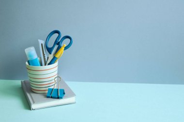 Kalem tutacağına malzeme ve mavi masaya defter yazmak. Mavi duvar arkaplanı. çalışma alanı
