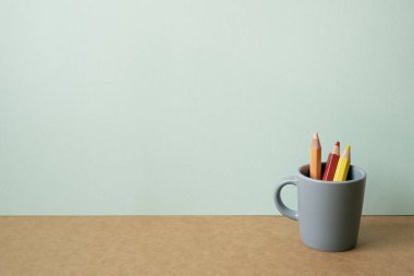 Kahverengi masadaki gri tutacaklı renkli kalemler. Nane yeşili duvar arkaplanı. Boşluğu kopyala