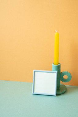 Mavi boş çerçeve ve nane yeşili masada mum. turuncu duvar arka planı. Boşluğu kopyala