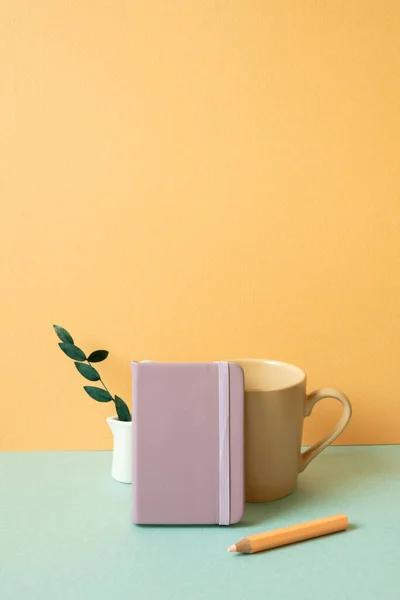 Purple notebook and mug cup, colored pencil, plant on mint green desk. orange wall background. copy space