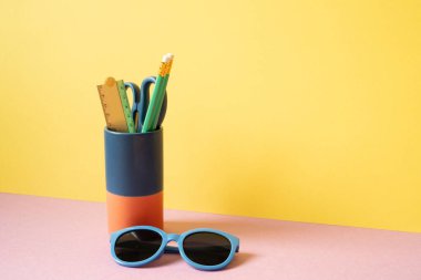 Kalem tutacağı ve güneş gözlükleri pembe masada. Sarı arka plan. çalışma alanı