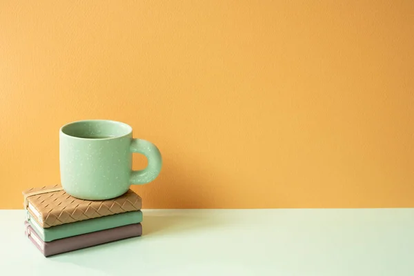Stack of notebook and mug cup on mint green desk. orange background. copy space
